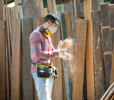 A man wearing wood safety equipment with piles of wood behind him